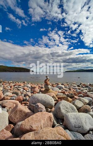 A small store cairn has been built from round granite stones on a rocky bay of the Baltic Sea on a sunny summer day.  Trollarviken near