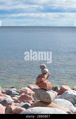 A small store cairn has been built from round granite stones on a rocky bay of the Baltic Sea on a sunny summer day.  Trollarviken near