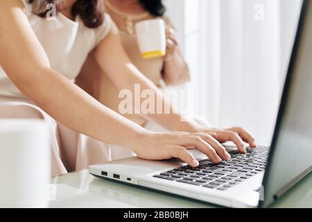 Hands of young woman typing on laptop when helping her senior mother to fill documents for bank Stock Photo