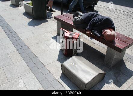 Cracow. Krakow. Poland. Street accordionist sleeps on the bench, his instrument standing by. Stock Photo