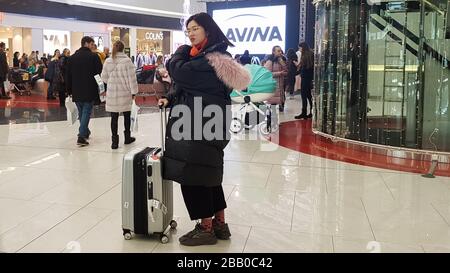 Ukraine, Kiev - February 25, 2020: A beautiful and young girl of Korean appearance with a suitcase at a duty-free airport or shopping center is Stock Photo