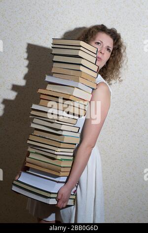Cheerful student holding huge pile of books standing in library Stock ...