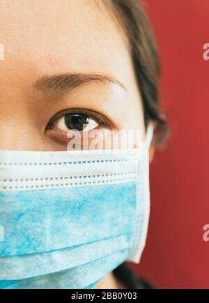 Coronavirus theme. Asian woman  wearing a mask to protect herself from getting infected on a red background. Stock Photo