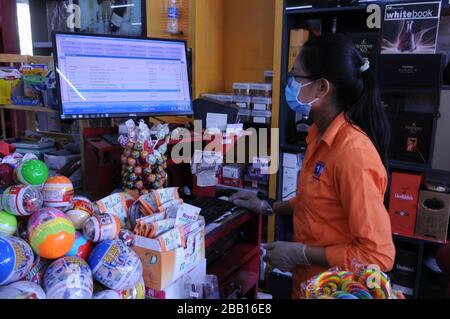 A supermarket cashier wears a face mask & sterile gloves at a checkout counter during the coronavirus pandemic. Phnom Penh, Cambodia. © Kraig Lieb Stock Photo