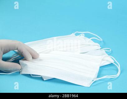 Hand with surgical gloves hanging Disposable Medical masks on blue background. Covid-19 and healthcare concept Stock Photo