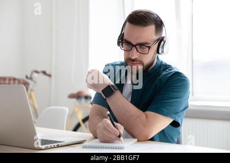 Focused man in headphones make notes working on laptop Stock Photo