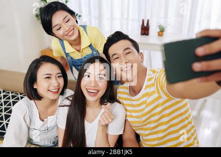 Happy beautiful young Asian woman making finger heart gesture when photographing with friends at party Stock Photo