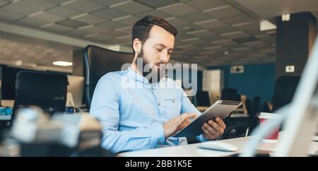 Caucasian businessman with beard browsing on his tablet while working in the office Stock Photo