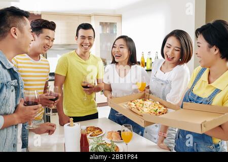 Group of happy friends gathered at kitchen table to have some drinks and est tasty pizza Stock Photo