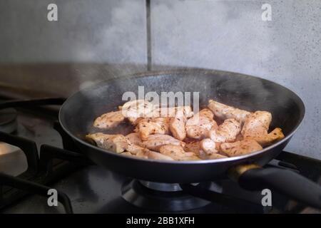 Close up of strips of chicken frying in pan with steam or smoke over the gas stove inside the kitchen. Stock Photo