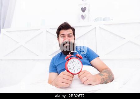 Time to wake up. Healthy habits. Wake up early every morning. Health benefits of rising early. Waking up early gives more time to prepare and be timely. Hipster bearded man in bed with alarm clock. Stock Photo