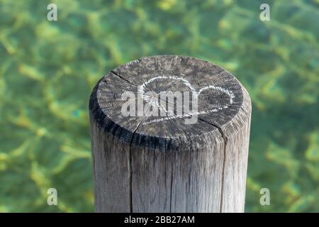 Chalk drawing of a heart symbol on a wooden pile of a pier. In the background green water. Concept for love, marriage, being together, valentines day. Stock Photo