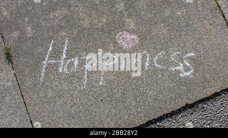 Word Happiness written on pavement with white chalk. With pink heart as dot for the i. Concept for postitive thinking, feeling happy, good vibrations. Stock Photo