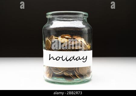 Coins in a jar with holiday text on a white label. Savings abstract concept. Copy space. Stock Photo