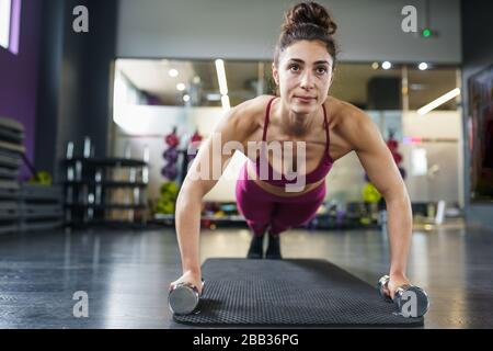 Woman doing push-ups exercise with dumbbell in a fitness workout Stock Photo
