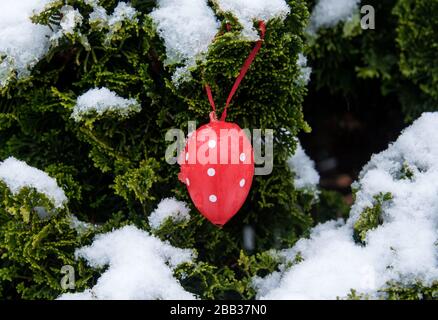 Hamburg, Germany. 30th Mar, 2020. A red Easter egg with white dots hangs in a front garden on a snow-covered tree branch. Credit: Daniel Bockwoldt/dpa/Ģ����ý Live News Stock Photo