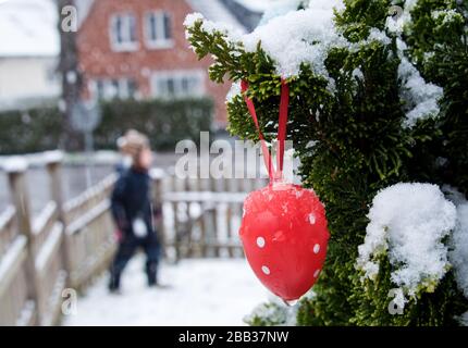 Hamburg, Germany. 30th Mar, 2020. A red Easter egg with white dots hangs in a front garden on a snow-covered tree branch. Credit: Daniel Bockwoldt/dpa/Ģ����ý Live News Stock Photo