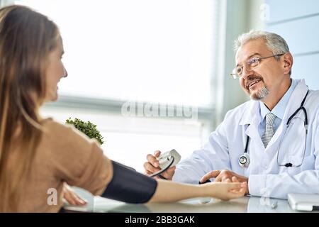 Young woman at the doctor appointment. The doctor measures the pressure of the patient Stock Photo