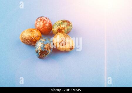 Five easter eggs painted in blue, green, red and yellow lie in a circle. Painted easter eggs on a blue background with light. Copy space. Stock Photo
