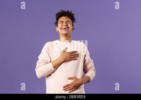 Portrait of cheerful, happy young hipster guy laughing out loud from hilarious joke, watching awesome stand-up performer, chuckle and touchign chest Stock Photo