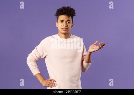 So what, why asking. Portrait of unbothered and careless, ignorant young man dont care on people rules, raising hand in dismay and confusion, being Stock Photo