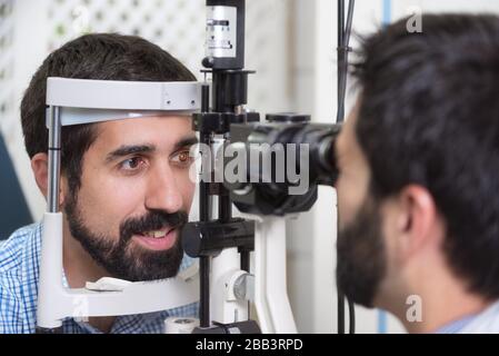 male doctor ophthalmologist is checking the eye vision of handsome young man in modern clinic. Doctor and patient in ophthalmology clinic.
