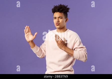 Portrait of funny and carefree young hispanic guy holding hands in martial arts attack pose, folding lips acting sassy and cool as imitating ninja Stock Photo