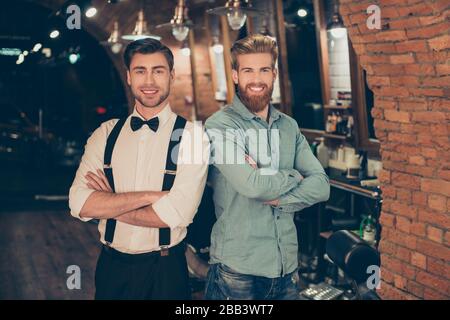 Welcome to barber shop! Red bearded handsome young man in a casual jeans outfit and attractive brunette dressed classy are standing with the crossed Stock Photo