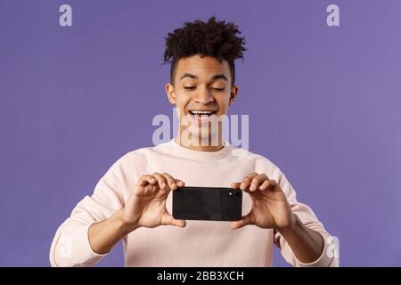 Portrait of amazed, excited young man seeing something interesting, stream concert to his internet social network profile, taking photo or recording Stock Photo