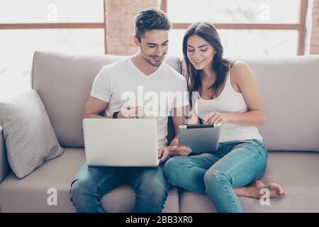 So easy! Excited beautiful happy couple is doing online shopping in internet. They are indoors at home on cozy couch in casual clothes, relaxing and Stock Photo