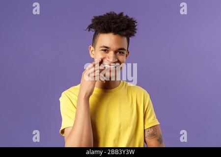 Close-up portrait of lovely young hispanic gay man with dreads, tattoos, touching lip sensually and flirty smiling, checking out someone really cute Stock Photo