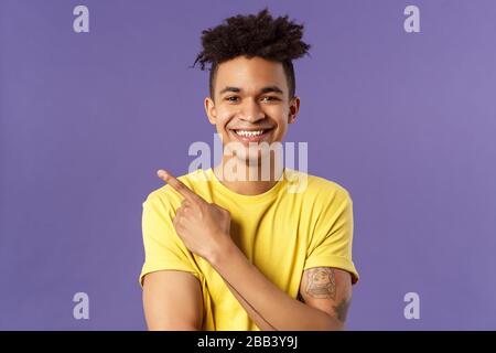 Close-up portrait of enthusiastic, happy young hipster male with dreads, beaming smile and pointing finger upper left corner, present cool product Stock Photo