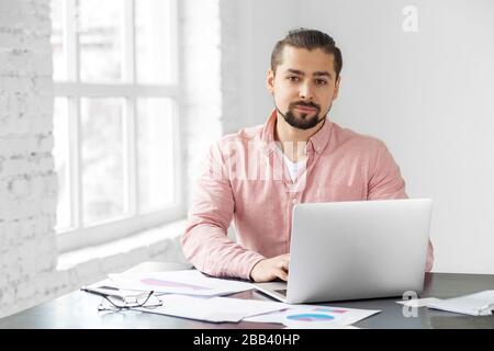 Young adult man working on a laptop. A man with a beard. Concept for business, corporation, work and making big money. Stock Photo