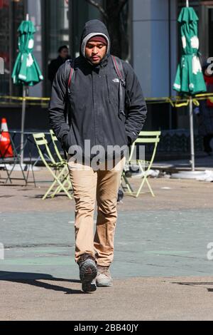 Young man walking with his hands in pocket and hood pulled up on a cold February day in Manhattan, New York City, United States of America Stock Photo