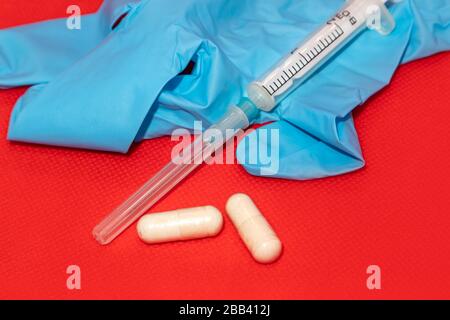 White 2 ml syringe macro on red surface, blue rubber glove, capsule supplement pills. Medicinal tool for injection, vaccine, cure Stock Photo