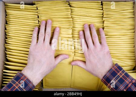 Male hands packing yellow bubble envelopes for shipping. Top view on four rows of padded mailers inside a cardboard box Stock Photo