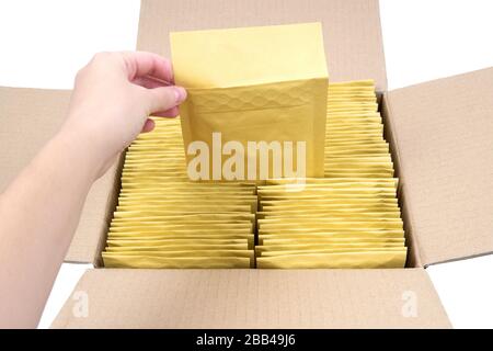 Female hand pulling a shipping envelope out of an opened box full of bubble mailers. Stock Photo