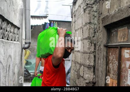 Quezon City. 30th Mar, 2020. A volunteer carries bags of relief goods as he participates in the distribution of aid from the local government at a slum area in Quezon City, the Philippines on March 30, 2020. Credit: Rouelle Umali/Xinhua/Alamy Live News Stock Photo