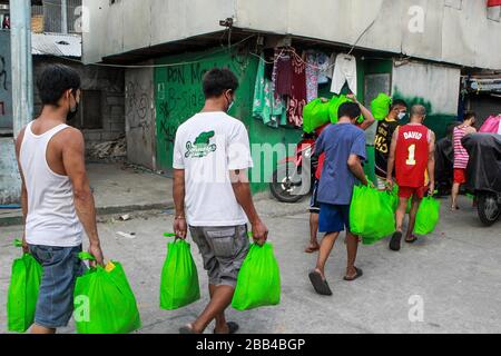 Quezon City. 30th Mar, 2020. Volunteers carry bags of relief goods as they participate in the distribution of aid from the local government at a slum area in Quezon City, the Philippines on March 30, 2020. Credit: Rouelle Umali/Xinhua/Alamy Live News Stock Photo