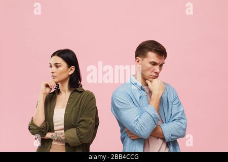 Waist up portrait of frustrated couple standing back to back against pink background, copy space Stock Photo