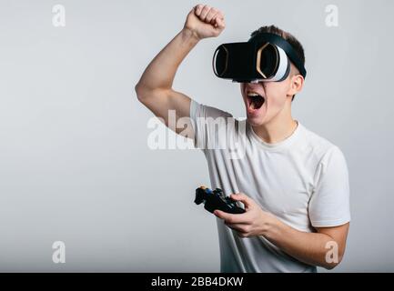 Man wearing virtual reality goggles and holding a gamepad while standing near white blackboard Stock Photo