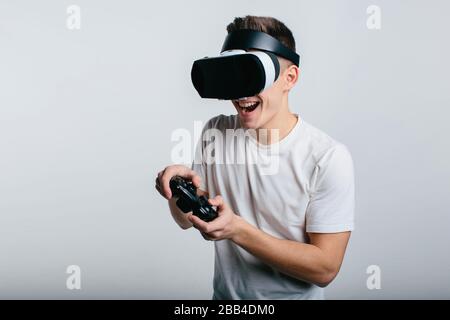 Man wearing virtual reality goggles and holding a gamepad while standing near white blackboard Stock Photo