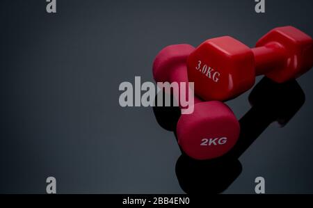 Red and dark pink dumbbells isolated on black background. 2, 3 kg dumbbells. Weight training equipment. Bodybuilding workout accessories. Equipment Stock Photo