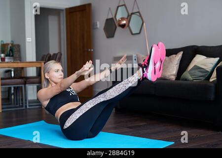 A Single Blonde female stretches as she exercises at home on a mat in the living room of her apartment Stock Photo