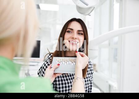 Beautiful young woman at dentist's office choose teeth color tone Stock Photo