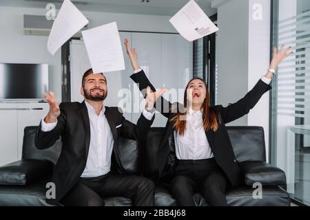 happy colleagues throwing business papers,The celebration of success. two young businessmen dropping documents and looking happy sitting at their desk Stock Photo