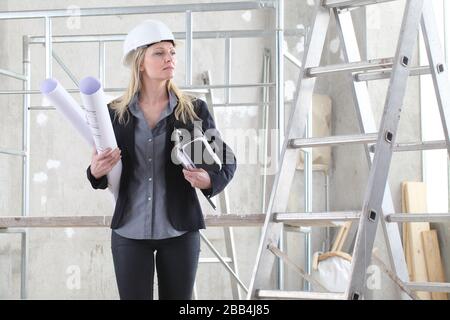 woman architect or construction engineer with virtual reality glasses wear helmet and holds blueprint inside a building site with ladder and scaffoldi Stock Photo
