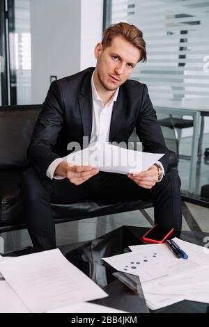 Developing a new idea...Handsome and successful businessman in stylish suit is thinking about something while sitting at office on sofa Stock Photo
