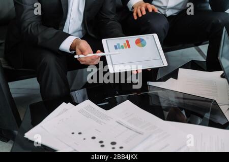 Business meeting. Teamwork. two Businessman sitting at table and working. Man shows tablet screen. Graphs, charts and diagrams on tablet screen. Onlin Stock Photo