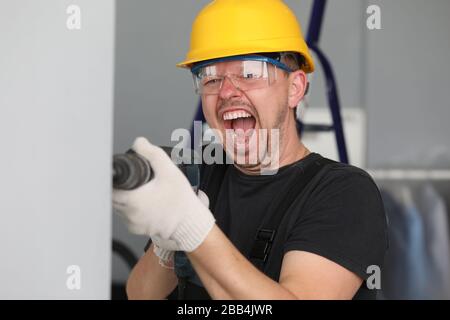 Male builder in helmet drills wall and screams Stock Photo